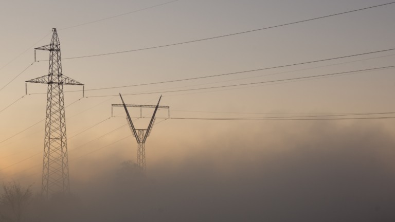 Electrical transmission towers connected by power lines in foggy conditions at dusk