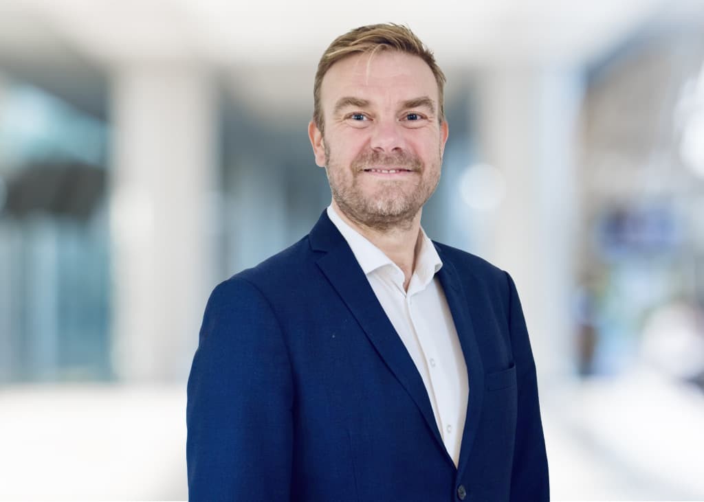 Peter Larsen, head shot of a smiling man wearing a suit