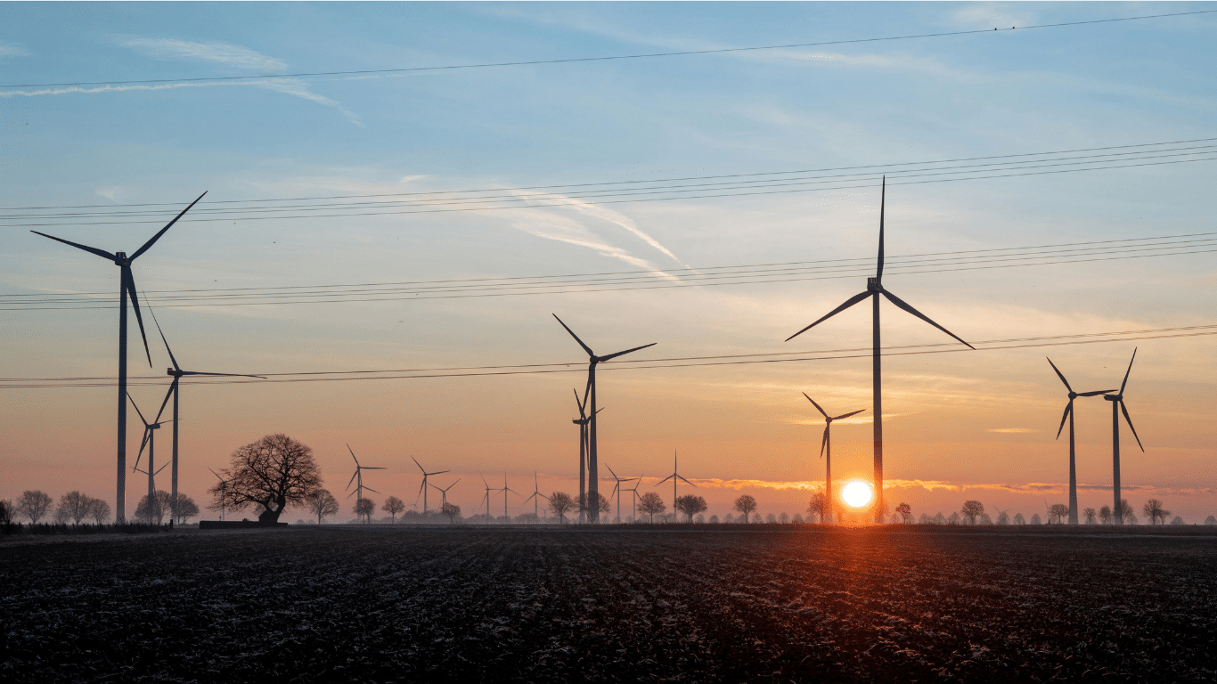 Wind turbines generating electricity at sunrise over a flat landscape, with power lines visible in the background.