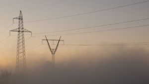 Electrical transmission towers connected by power lines in foggy conditions at dusk